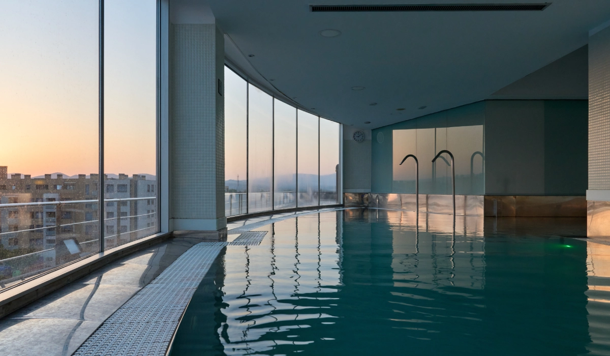 Piscina interior con grandes ventanales y vista al atardecer.