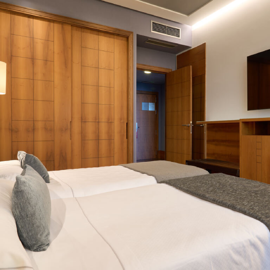 Habitaci&oacute;n de hotel con dos camas y puerta de madera abierta.