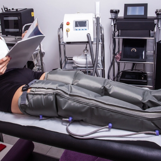 Persona recibe presoterapia mientras lee una revista en una sala de tratamientos.