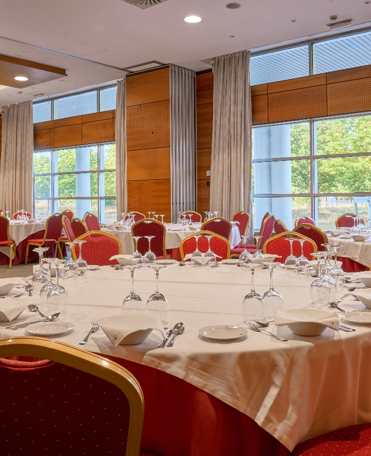 Mesas redondas con manteles blancos y sillas rojas en un sal&oacute;n iluminado.