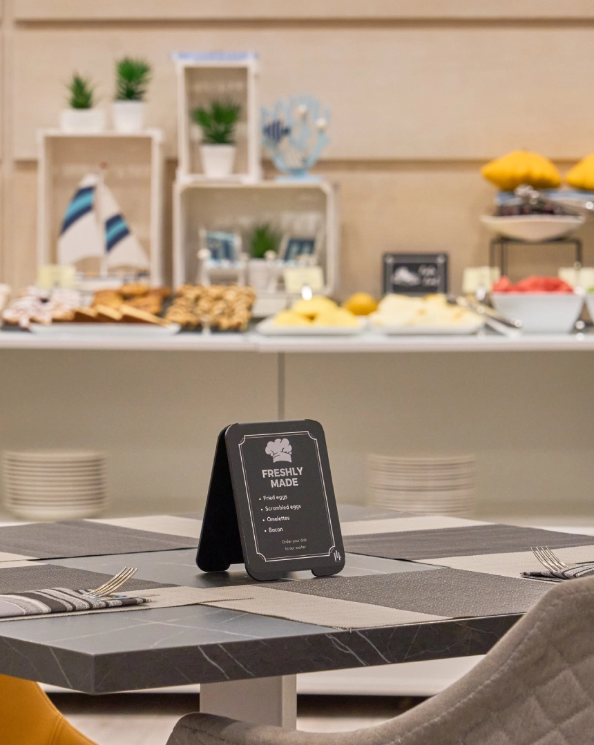 Mesa con men&uacute; y desayuno buf&eacute; al fondo.