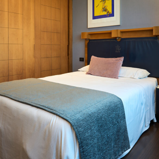 Cama grande en habitaci&oacute;n con armario de madera y cuadro amarillo en la pared.