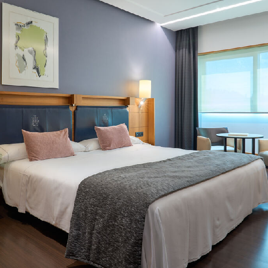 Habitaci&oacute;n de hotel moderna con cama grande, l&aacute;mpara y ventana.