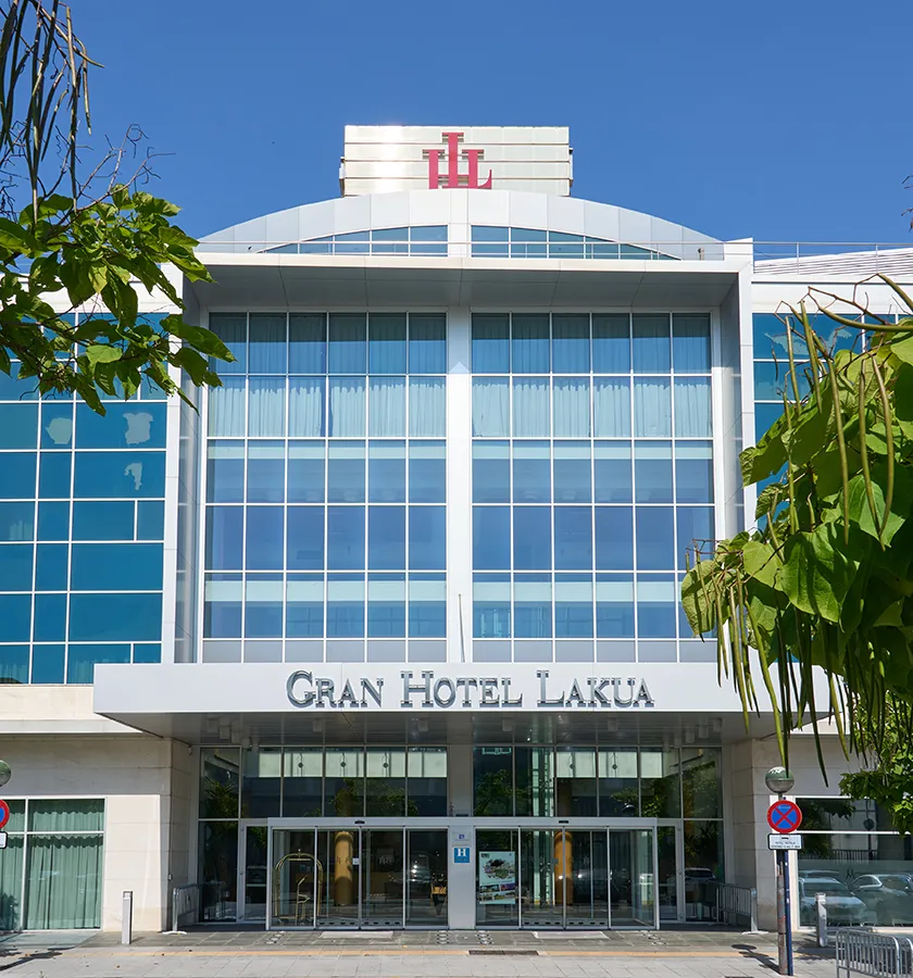 Fachada del Gran Hotel Lakua con cielo despejado y &aacute;rboles alrededor.