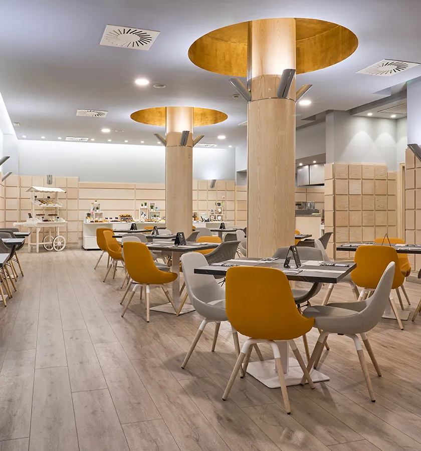 Sala de restaurante moderna con sillas amarillas y grises, y decoraci&oacute;n luminosa.