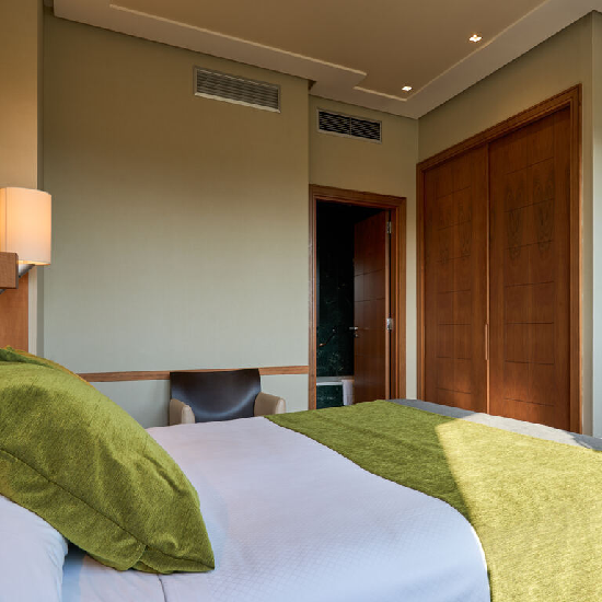 Habitaci&oacute;n moderna con cama blanca y manta verde, silla y armario de madera.