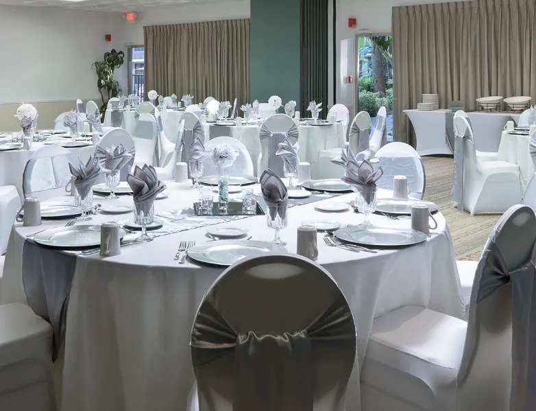 Un sal&oacute;n de eventos con mesas redondas cubiertas de manteles blancos y sillas decoradas.