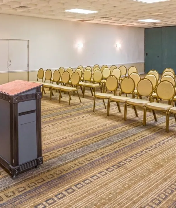 Aula vacía con sillas alineadas y un podio al frente en una sala de conferencias iluminada.