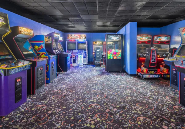 Sala de videojuegos retro con m&aacute;quinas arcade y alfombra de dise&ntilde;o colorido.