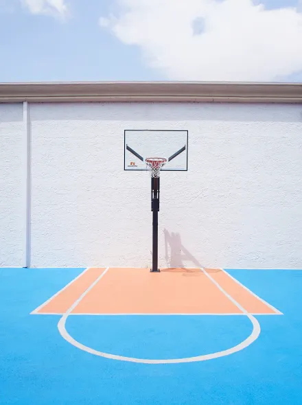 Cancha de baloncesto de colores azul y naranja con un aro frente a una pared blanca.