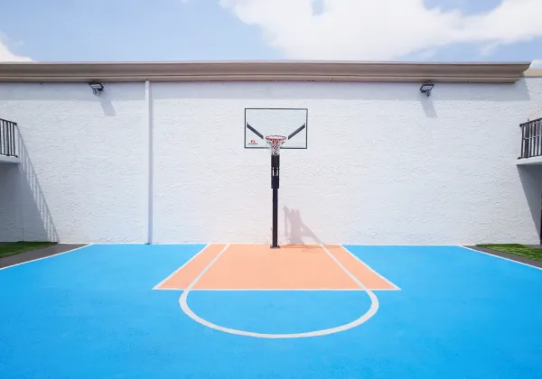 Cancha de baloncesto al aire libre con suelo azul y zona naranja, frente a una pared blanca.