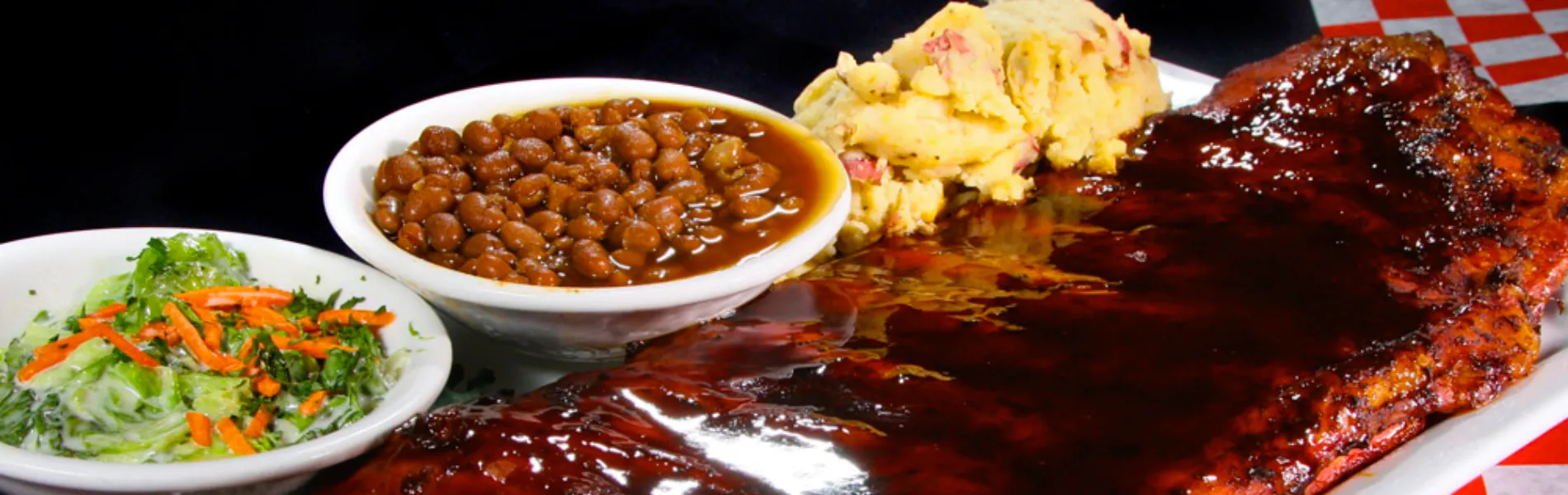 Costilla asada con ensalada, frijoles y puré de papas servidos en un plato blanco.