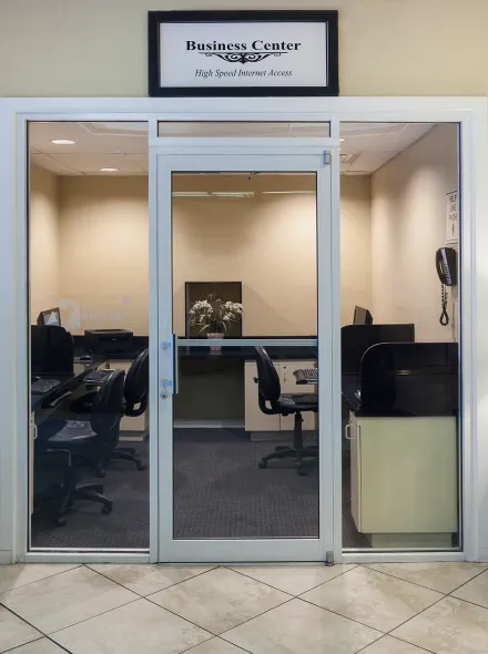 Puerta de cristal a un centro de negocios con escritorios y sillas. Cartel: "Business Center".