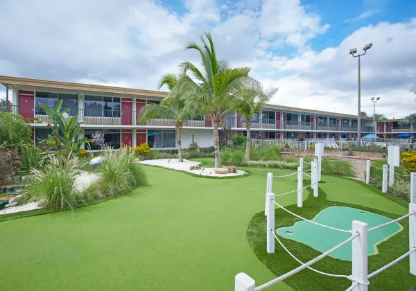 &Aacute;rea de minigolf con palmeras y c&eacute;sped en un complejo hotelero bajo un cielo nublado.