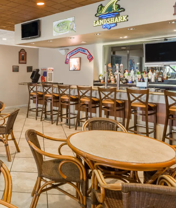 Bar con sillas de madera, mesas redondas y letreros decorativos en las paredes.