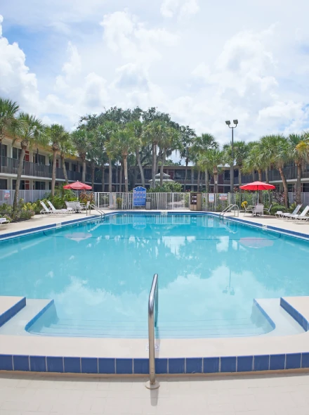 Piscina al aire libre rodeada de palmeras y tumbonas bajo un cielo parcialmente nublado.