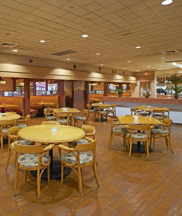 Restaurante vac&iacute;o con mesas y sillas de madera, y cabinas al fondo.