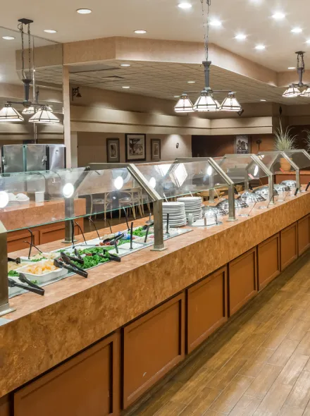 Buffet con iluminaci&oacute;n suave, estaciones de comida vac&iacute;as y vajilla apilada en un restaurante.