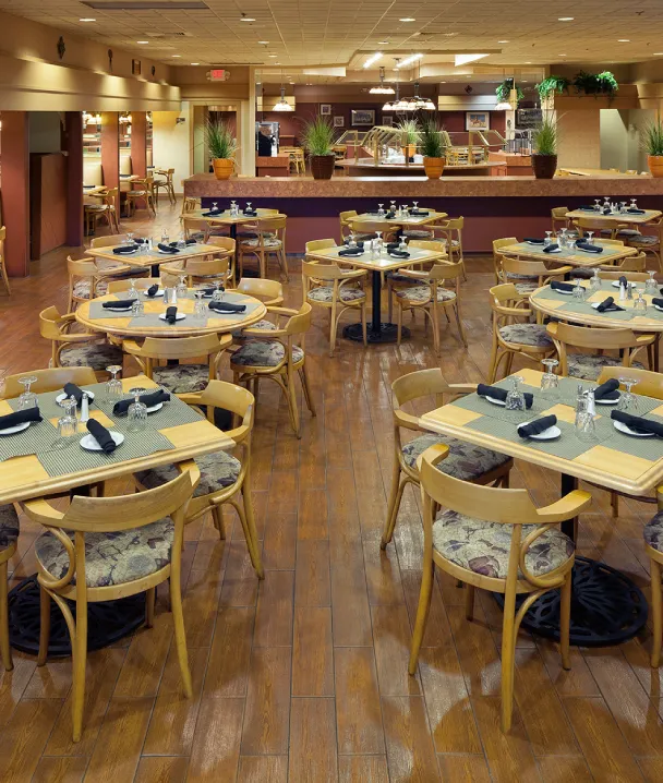 Restaurante vac&iacute;o con mesas de madera, cubiertos y plantas decorativas. Ambiente c&aacute;lido y acogedor.