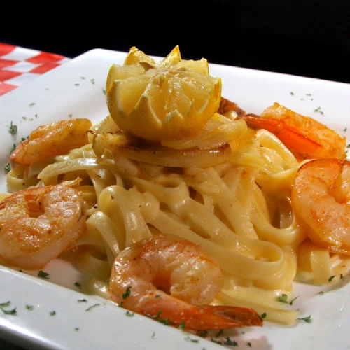 Plato de pasta fettuccine con camarones y limón decorativo en un plato blanco.