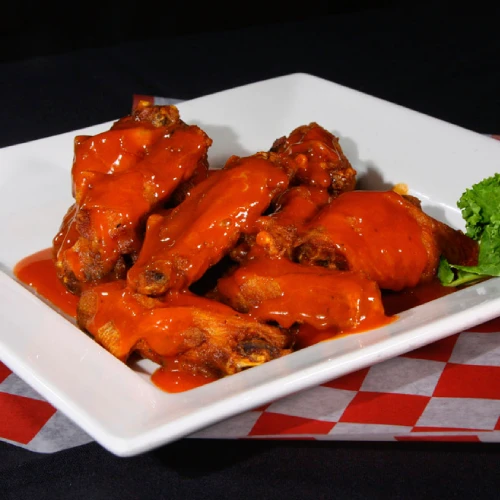 Alitas de pollo con salsa buffalo en un plato blanco, sobre un mantel a cuadros rojo y blanco.