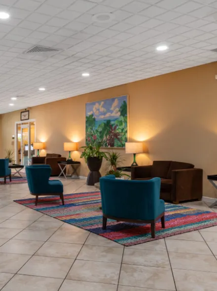 Sala de espera con sillones azules, alfombra colorida y pintura en la pared.