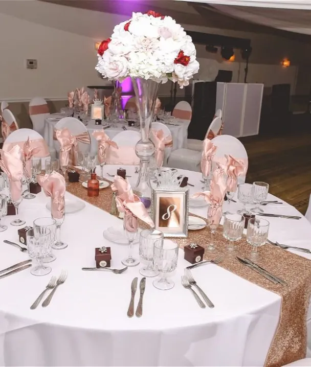 Mesa decorada con flores y cubiertos para un evento elegante, sillas con lazos y centro de mesa.