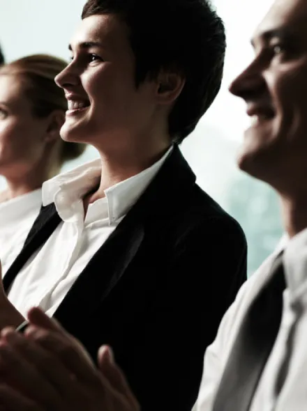 Personas aplaudiendo y sonriendo, vestidas formalmente.