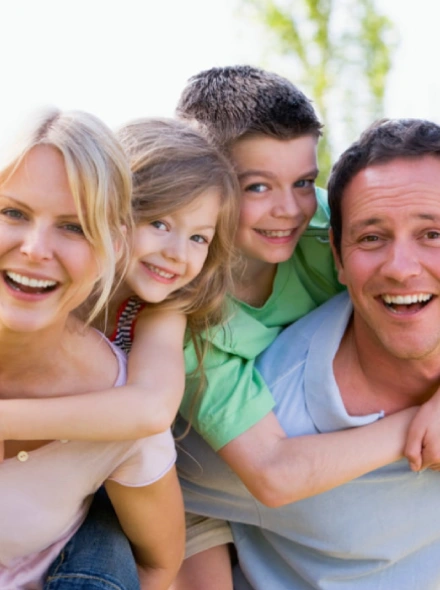 Familia feliz sonriendo al aire libre; dos adultos y dos ni&ntilde;os juntos.