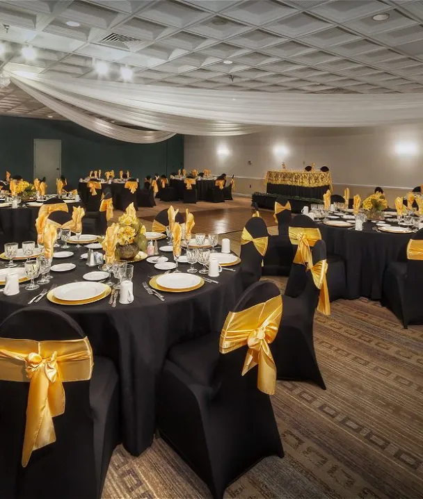 Salón de eventos decorado con mesas y sillas negras con lazos dorados.