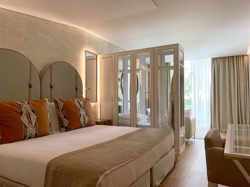 Modern hotel room with a large bed, decorative pillows, and mirrored wardrobe.