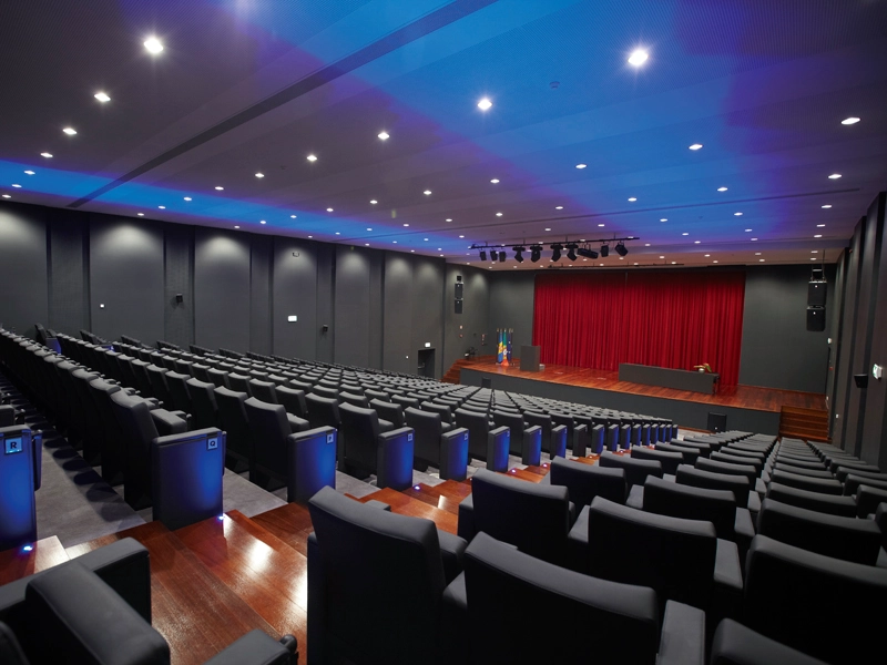 Empty auditorium with red curtains and rows of black seats.