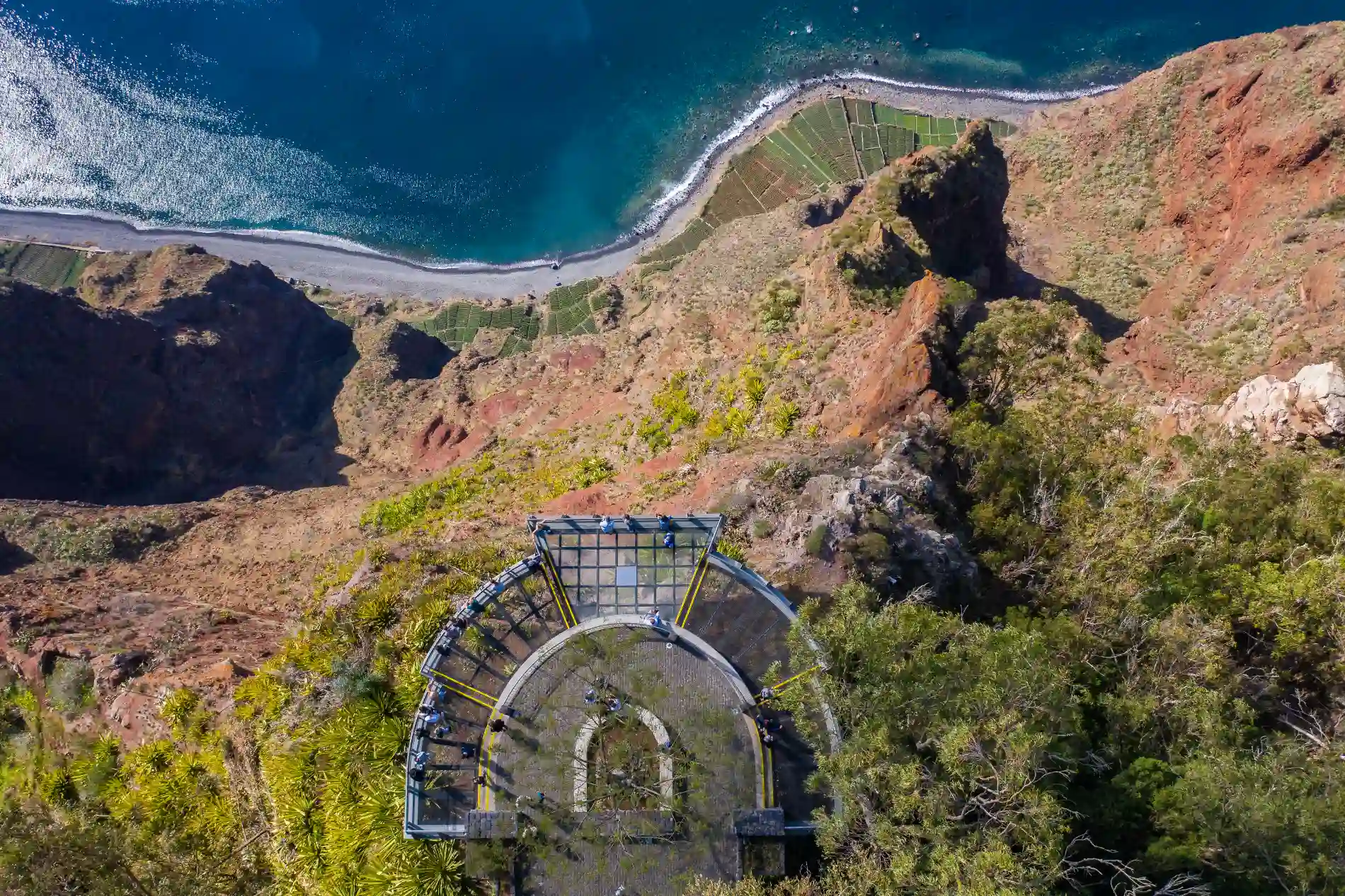 Glass viewing platform overlooking a cliff and ocean with greenery below.