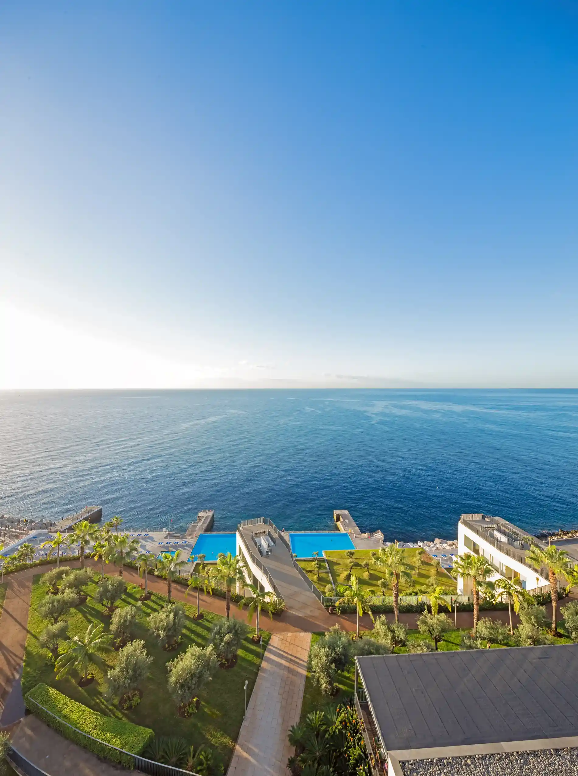 Coastal resort with blue ocean, pool, and lush greenery under a clear sky.