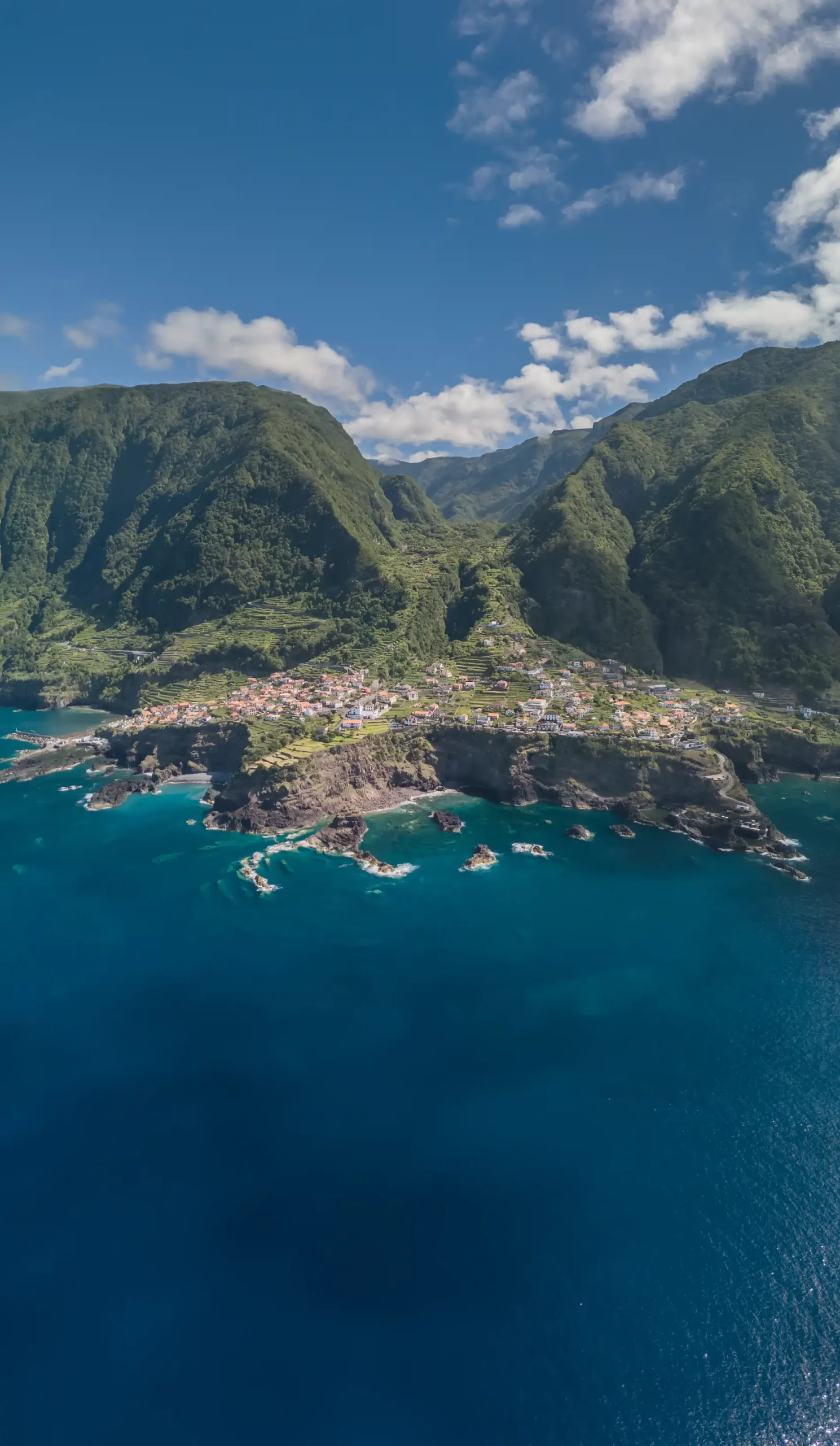 Coastal village by lush green mountains and blue ocean under a clear sky.