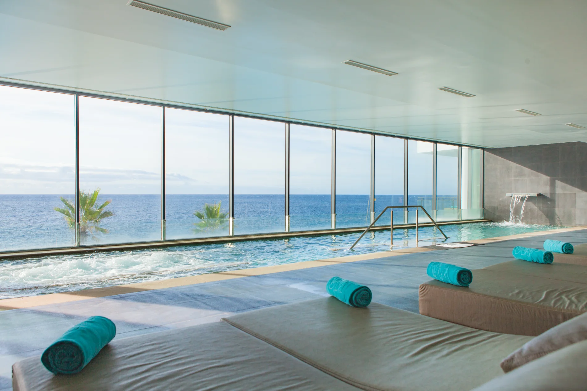 Indoor pool with ocean view and loungers, towels placed neatly on top.