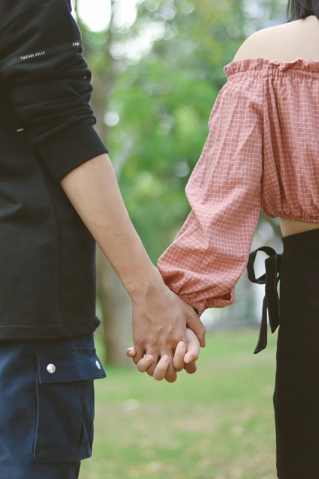 Two people hold hands outdoors, wearing casual clothing.