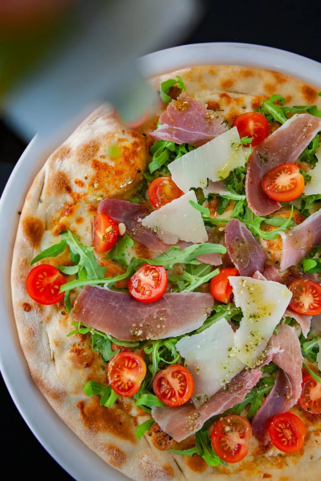 Pizza with arugula, prosciutto, parmesan, and cherry tomatoes.