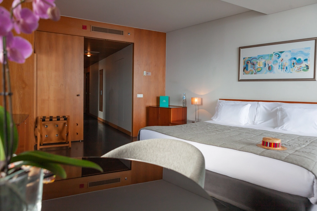 Modern hotel room with a large bed, artwork, and orchid in foreground.