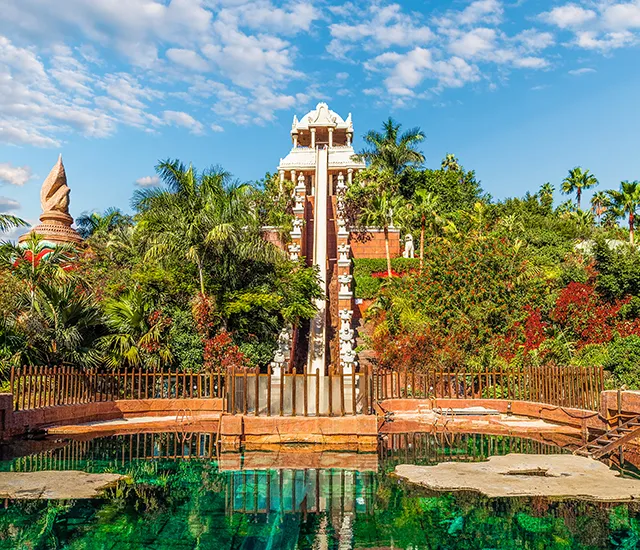 A temple-themed water slide surrounded by lush greenery and water.