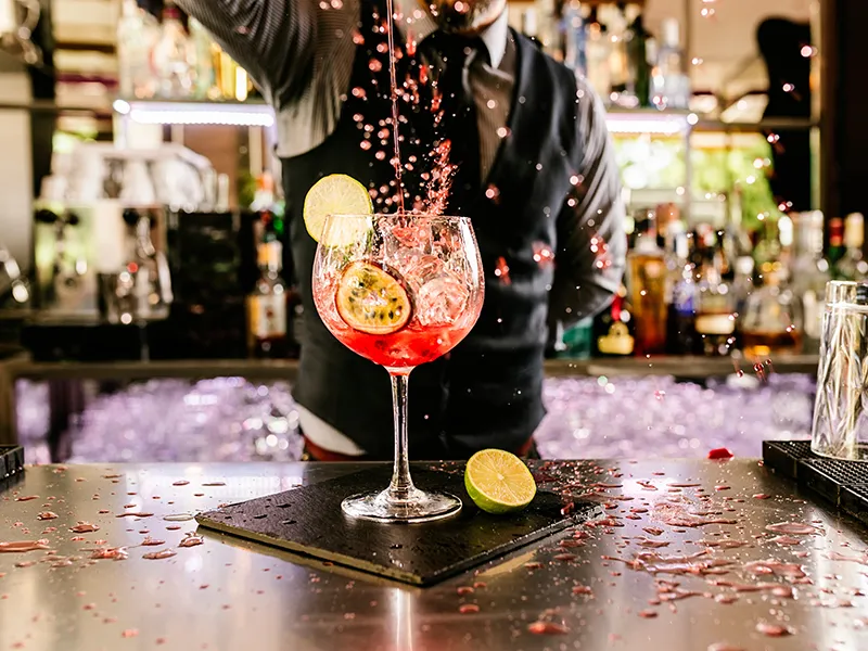 Bartender creating a vibrant, splashing cocktail with lime and passion fruit garnish.