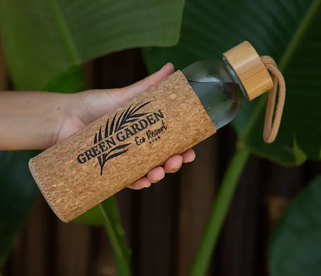 A hand holds a cork-covered bottle labeled "Green Garden Eco Resort."