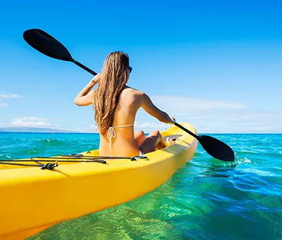 Woman kayaking on clear turquoise water under a bright blue sky.