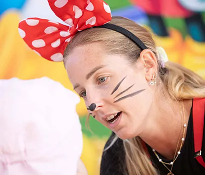 Person with mouse ears and face paint talking to a child in a pink hat.