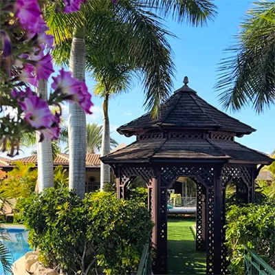 Tropical gazebo with flowers and palm trees under a clear blue sky.