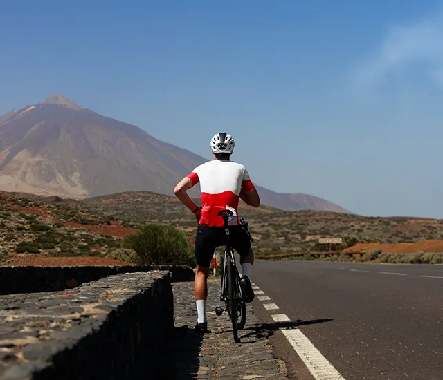 Cyclist rests on roadside with mountain view.