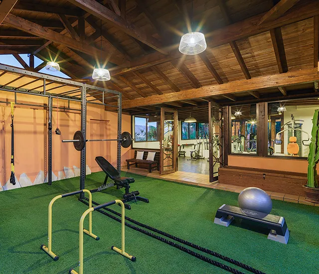 Spacious gym with equipment, green floor, wooden ceiling, and bright lighting.