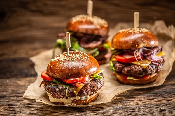 Three gourmet burgers with lettuce and tomatoes on a wooden surface.