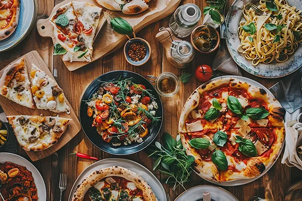A table full of assorted pizzas and pasta dishes with fresh ingredients.