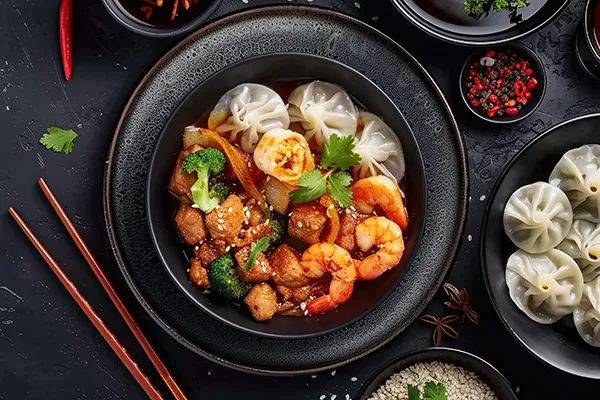 A dish with shrimp, tofu, broccoli, and dumplings on a black plate.